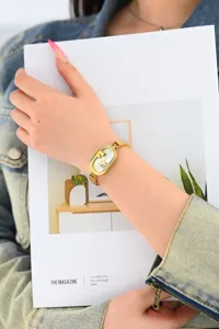 Primer plano de un reloj de mujer ovalado dorado con pedrería y fina correa de acero.