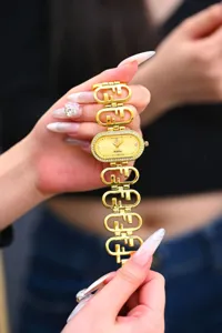 Close-up detail of luxury gold oval quartz watch with diamond bezel and F-link bracelet.
