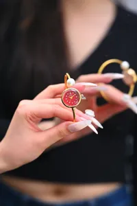 Primo piano dettaglio orologio bracciale da donna dorato con quadrante rosso e perla.