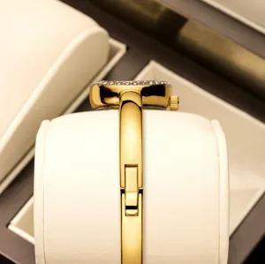 Gold tone quartz bangle watch for women featuring elegant diamond bezel and secure clasp.