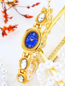Gold-tone women's vintage oval watch with blue dial, rhinestone chain strap and pearl props.