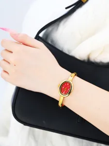 Gold-tone oval bangle watch detail with striking red dial and elegant minimalist design.