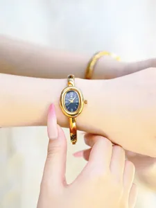 Elegant gold oval bangle watch for women, vintage quartz wristwatch with black dial.