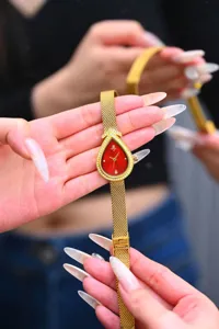 Goldene tropfenförmige Quarzuhr Detail mit rotem Zifferblatt und funkelnder Lünette.