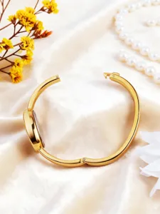 Close-up detail of the elegant gold oval bangle watch displayed on silk with pearls.