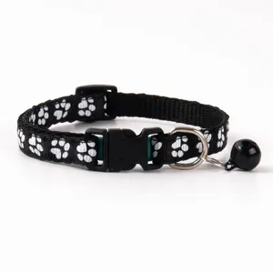 Close up detail of black pet collar featuring white paw print pattern and safety bell.
