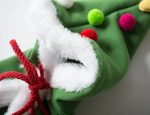 Close-up of green pet Christmas tree cape with white plush trim and colorful pom-poms.
