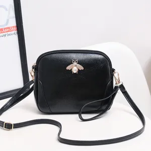 Vista detallada del bolso cruzado de cuero negro con abeja dorada y perla elegante.