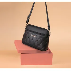 Detail view of black quilted crossbody bag featuring heart embroidery and bow hardware.