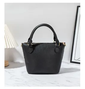Black leather handbag detail showing fine texture, gold hardware zipper and sturdy double handles.