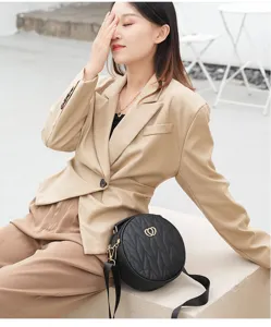 Stylish black round quilted crossbody bag with wide strap and chic metallic heart buckle design.