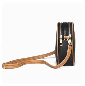 Side view detail of black vertical crossbody phone bag with brown piping and dual zippers.