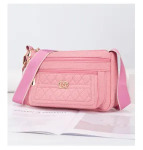 Gros plan du sac bandoulière en toile rose montrant le logo en métal et les poches zippées.
