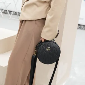Black round quilted crossbody bag for women with wide strap and gold heart hardware.