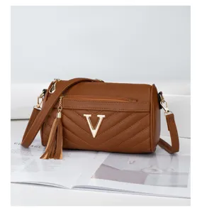 Brown cylinder shoulder bag with gold V buckle and tassel charm for women fashion chic daily.