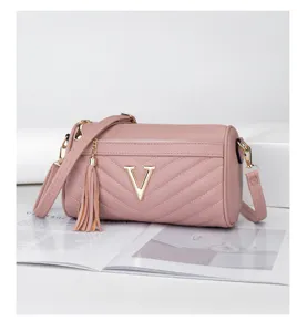 Detailed shot of stylish pink quilted cylinder crossbody bag with gold V logo and cute tassel.