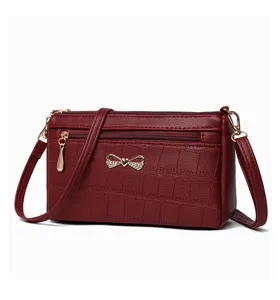 Dettaglio della borsa a tracolla rosso vinaccia effetto coccodrillo con fiocco dorato e zip.
