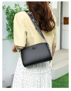 Detailed view of black leather shoulder bag with wide branded strap and casual style.