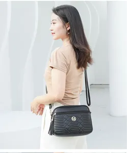 Sac bandoulière noir en cuir avec matelassage géométrique et pompon élégant chic.