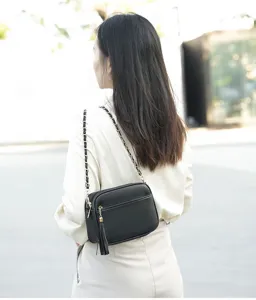 Black pebbled leather crossbody bag with chain strap, front zipper pocket and tassel detail.