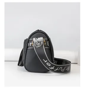 Detail view of a black cylinder crossbody shoulder bag with wide strap and tassel decoration.