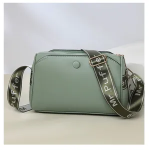 Close-up detail of green women crossbody bag with wide printed strap and metallic hardware.