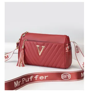 Detailed shot of red cylinder crossbody bag with metal V logo, chevron quilting and strap.