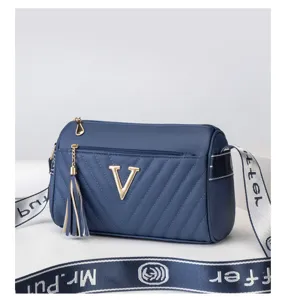 Detailed view of the stylish blue cylindrical crossbody bag with metal V logo and wide strap.