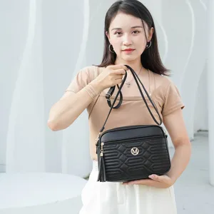 Sac a bandouliere noir elegante pour femme avec logo metal M et pompon pour automne.