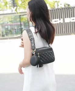 Detailed view of the black quilted crossbody bag featuring a wide strap, tassel, and coin purse.