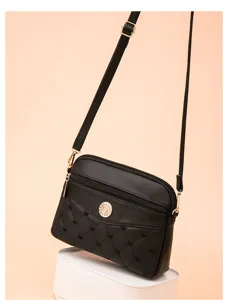 Black quilted crossbody bag detail showing heart embroidery, zipper pocket and chic hardware.