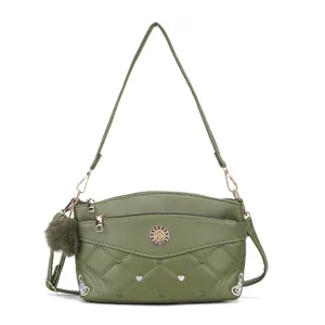Green quilted crossbody bag detail with fluffy pompom charm and metal orb logo for women.