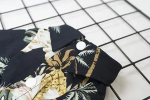 Close-up detail of tropical palm leaf and pineapple print pet dog shirt with collar and white buttons.