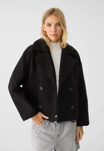 Detail view of black double-breasted short wool coat worn by model, stylish lapel design.