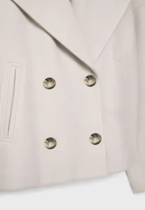 Detailed shot of women's short woolen coat featuring lapel collar and tortoiseshell buttons.