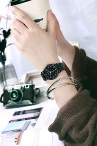 Close-up detail of minimalist black dial quartz watch with black strap worn on wrist.
