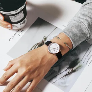 Chic quartz watch with minimalist white dial and black strap, paired with delicate leaf bracelets.
