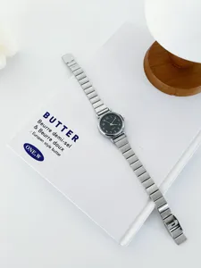 Close-up view of a minimalist silver metal watch with black dial placed on a white book prop.