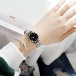 Closeup of a minimalist women quartz watch with black dial and silver mesh strap and bangle.