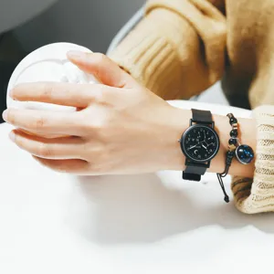 Close-up detail of black quartz watch with constellation dial and beaded bracelet on wrist.
