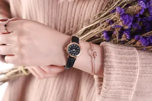 Detail shot of a women's vintage quartz watch with black dial and leather strap, worn on wrist.