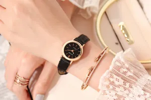 Detail close-up of a women's small black dial quartz watch with slim leather strap worn on wrist.