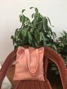 Vista detallada de un bolso tote de lona rosa liso en una silla de mimbre con plantas verdes.