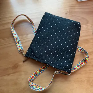 Élégant sac bandoulière noir avec motif à pois et sangle tissée ethnique colorée et vive.