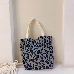 Λεπτομέρεια τσάντας tote από κοτλέ με μπλε λεοπάρ σχέδιο και άνετες λευκές λαβές.