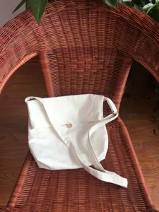 Detailaufnahme einer schlichten weißen Segeltuch Umhängetasche mit Klappe und Holzknopf.