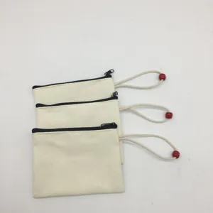 Close-up detail shot of three stacked blank canvas zipper pouches with red bead wristlet straps.