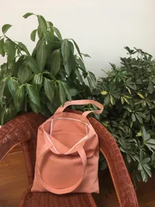 Vista detallada de bolso tote de lona rosa liso colocado en silla de mimbre con plantas.
