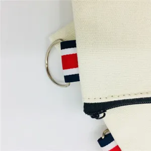 Canvas zipper pouch detail with metal D-ring and striped ribbon loop, ideal for daily use.