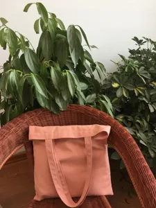 Vista detallada de un bolso tote de lona rosa sencillo sobre una silla con plantas.